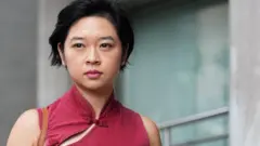 鄭嘉如身穿棗紅色旗袍風上衣抵達香港東區裁判法院,神情嚴肅(10/9/2026)