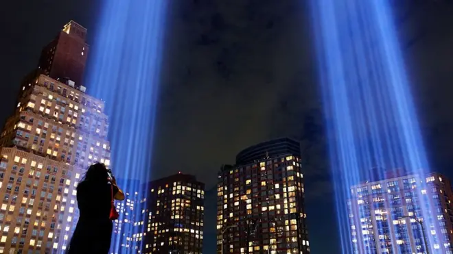 Một người phụ nữ chụp ảnh hai luồng sáng tạo nên tác phẩm "Tribute in Light" (Tưởng niệm bằng Ánh sáng) trên bầu trời Manhattan, chuẩn bị cho lễ tưởng niệm 25 năm vụ tấn công Trung tâm Thương mại Thế giới vào ngày 9/9/2026 tại Thành phố New York.